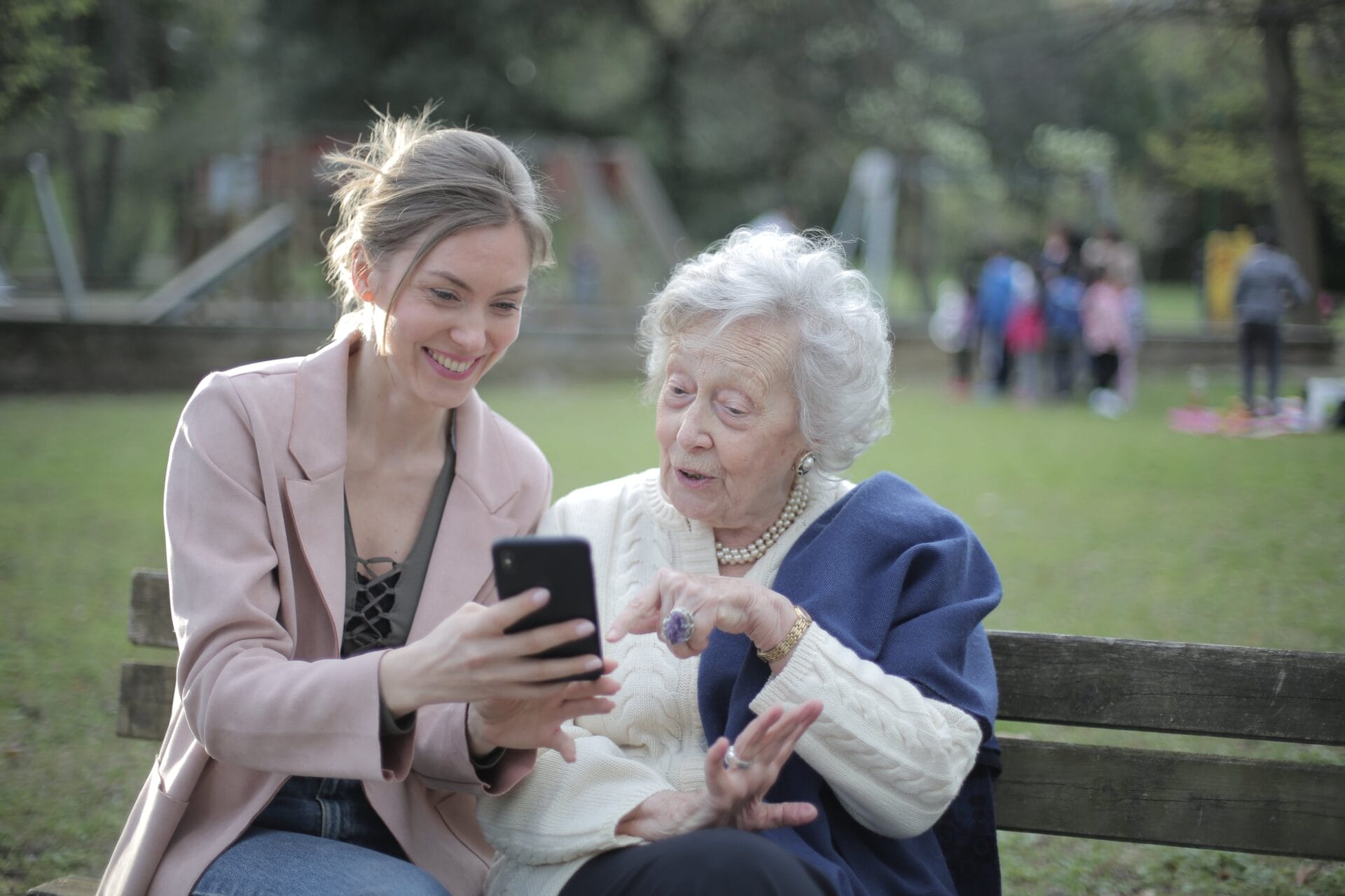 A younger person pointing to a cell phone with a senior citizen.
