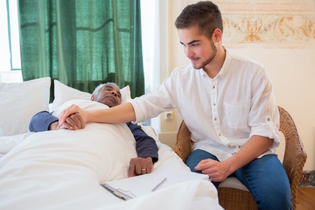 Young man holding older man's hand while older man is in bed