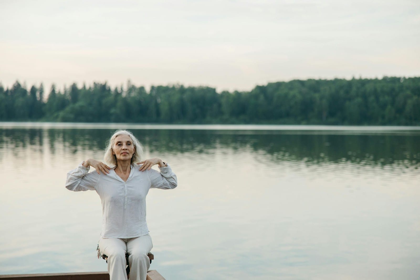 An elderly woman stretching near a lake