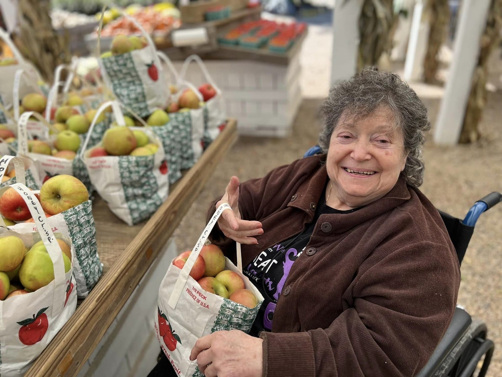 An elderly woman in a wheelchair, smiling with a bushel of apples