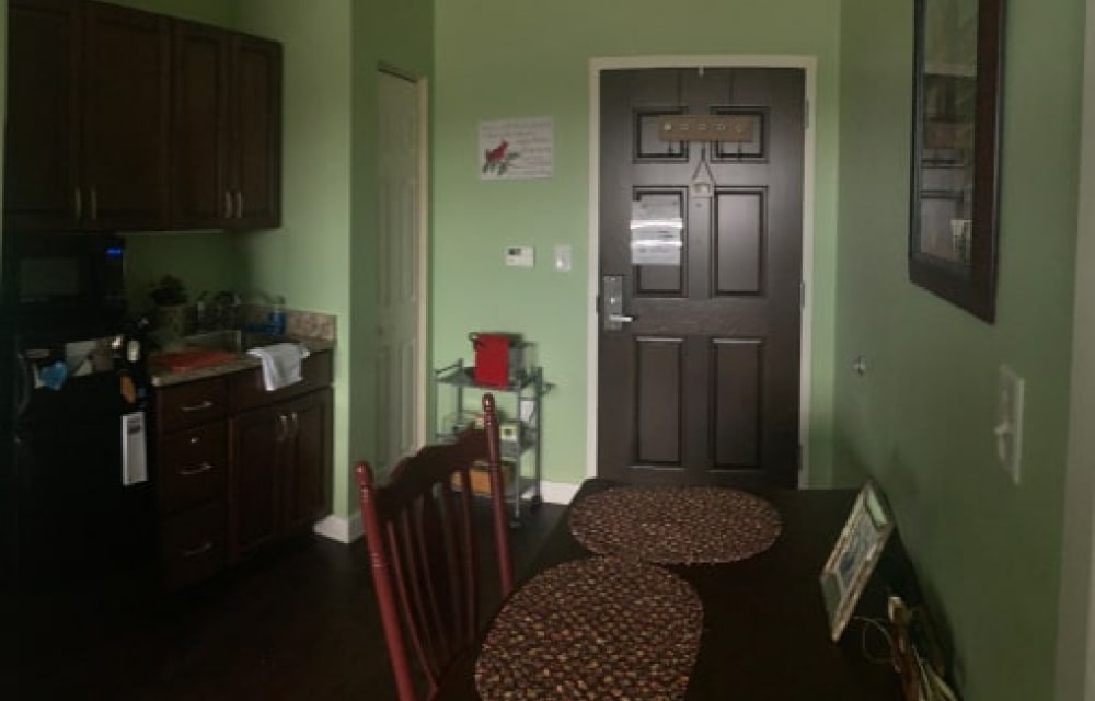 A small green room with a kitchen and a wooden table for old people