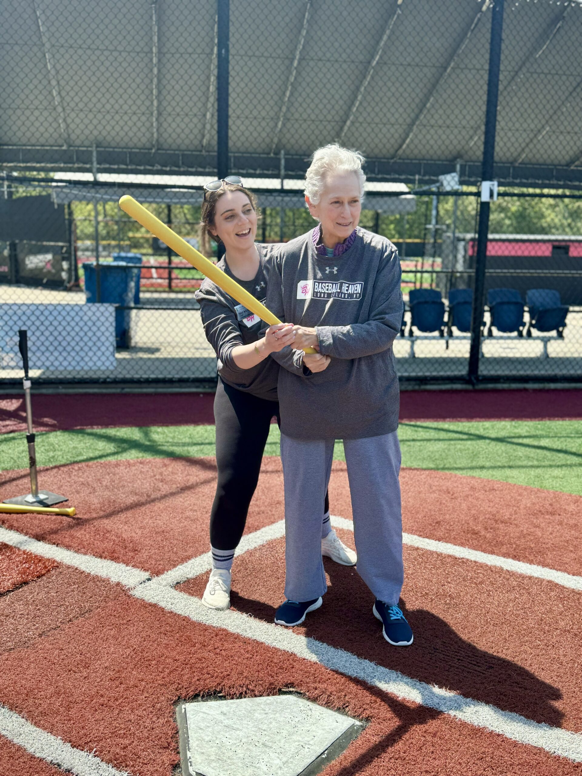 A woman helping an elderly lady play baseball