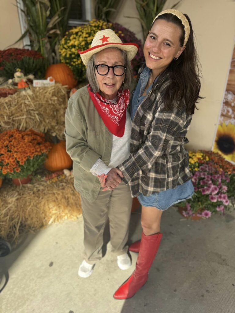 A picture of an assisted living resident smiling in cowboy clothing with an assisted living staff member