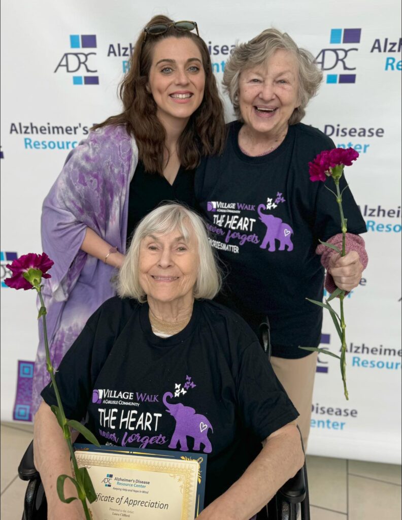 A picture of a staff member and memory care residents in front of an Alzheimer's poster backdrop