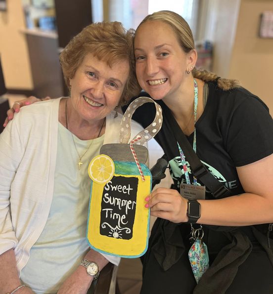 A caregiver smiling with her arm draped around the shoulder of an assisted living resident