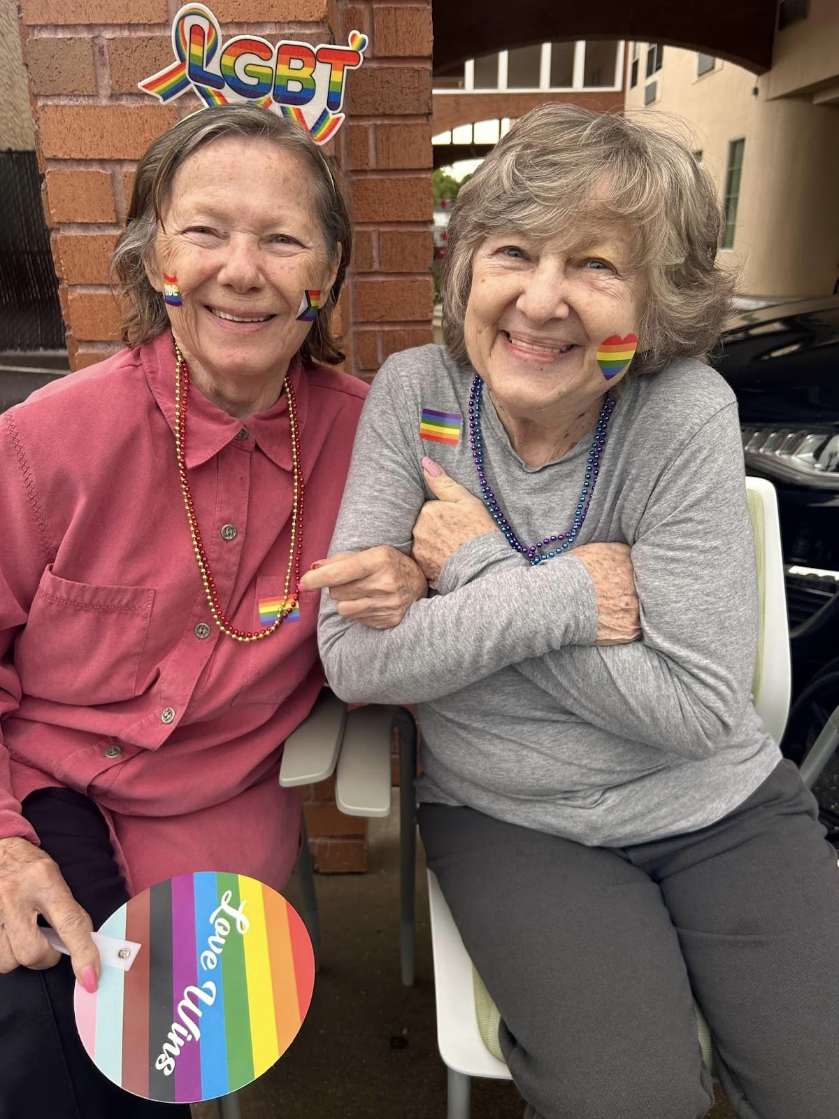 Two assisted living residents smiling with each other while wearing LGBTQ-friendly decorations