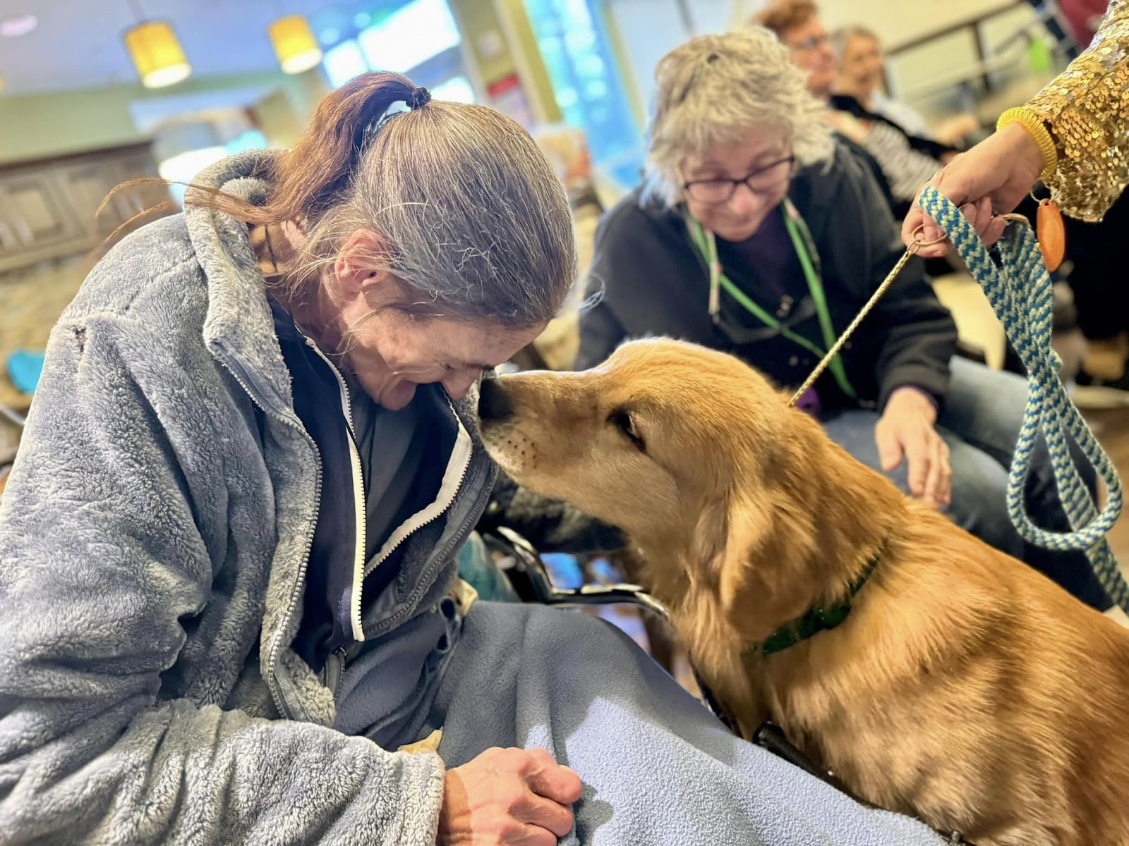 An assisted living and/or nursing home resident placing their head to the nose of a golden retriever.