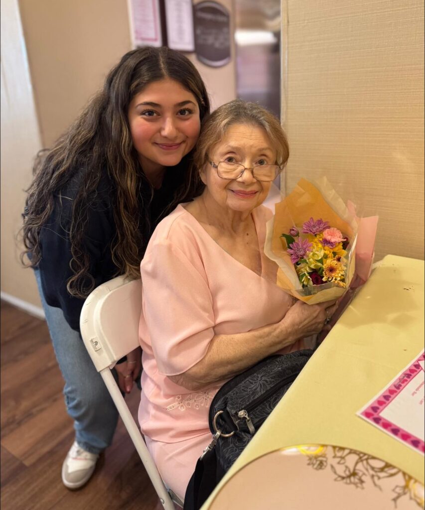 A picture of an elderly lady smiling with flowers with a younger person