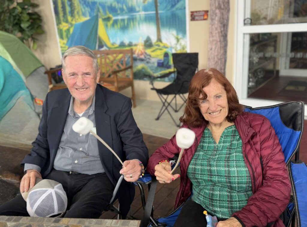 Two older adults sitting in a chair with marshmallows on a stick